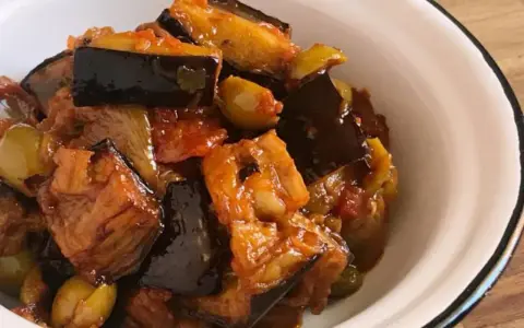 Un plato de caponata siciliana, con berenjenas, aceitunas y tomate, servido en un cuenco blanco.