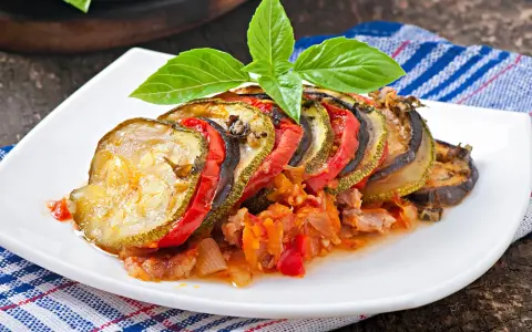 Ratatouille con rodajas de calabacín, berenjena y tomate, decorado con albahaca. Los ingredientes ratatouille se ven tiernos y jugosos.