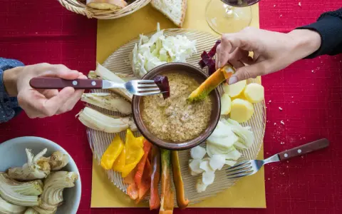 Un gruppo di mani intinge verdure nella bagna cauda, un piatto conviviale.