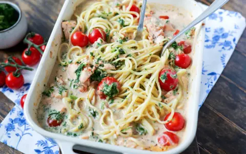 Cremige Lachs Spinat Pasta mit Kirschtomaten in einer Auflaufform, serviert mit zwei Gabeln.