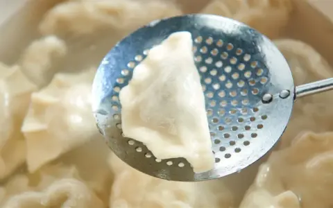 Pieróg wyjmowany łyżką cedzakową z gotującej się wody.
