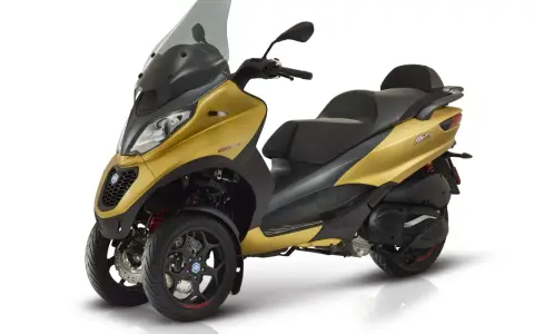 Złoty Piaggio MP3 500, trójkołowy skuter, gotowy do osiągnięcia swojej maksymalnej prędkości.