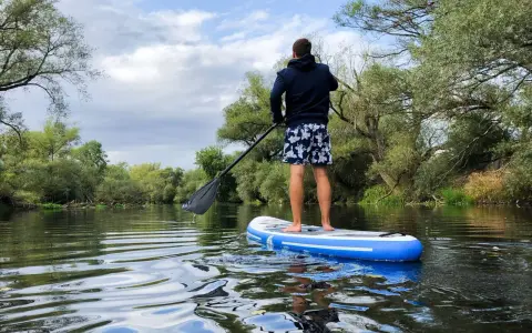 Mann auf SUP-Tour auf einem ruhigen Fluss, umgeben von üppiger Vegetation.