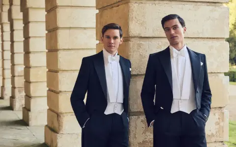 Two men in formal attire, a white tie event, stand by a stone colonnade.