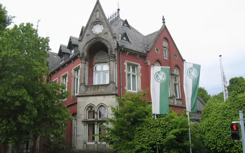Die Kaiservilla in Minden, ein rotes Backsteingebäude mit Türmchen und zwei GWD-Fahnen, umgeben von üppigem Grün.