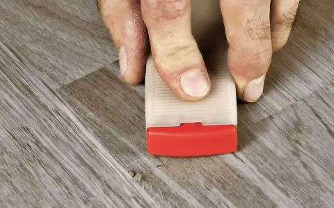 Fingrar använder en kil för att laga laminatgolv.