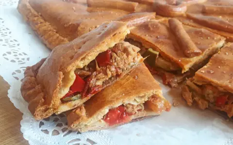 Una deliciosa empanada de carne, cortada en porciones, revela su jugoso relleno de carne deshebrada y pimientos rojos.