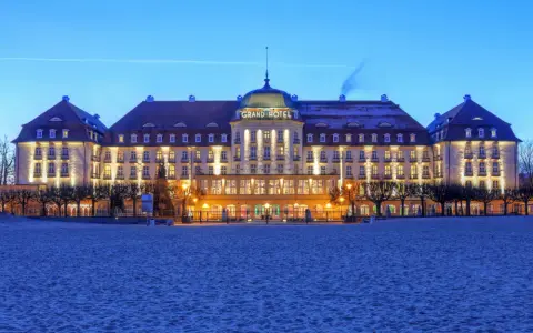Elegancki Grand Hotel, część sieci luksusowych hoteli, lśni nocą na tle plaży.