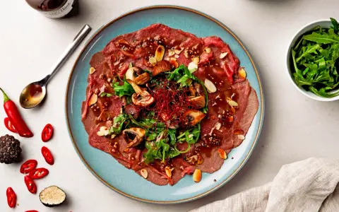 Carpaccio vom Rind mit Pilzen, Rucola und Mandeln, garniert mit Chili und Trüffel. Ein Gericht, das zeigt, was ist Carpaccio.