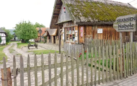 Drewniane chaty ze słomianymi dachami w skansenie w Nadolu. W oddali widać wóz.