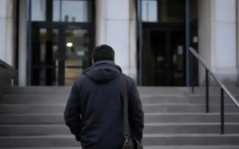 Mężczyzna w ciemnej kurtce wchodzi po schodach. W ręku trzyma torbę, jakby niósł ważny, żelazny list.