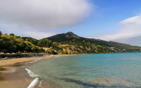 Piękna plaża Tragaki Zakynthos z turkusową wodą, zielonymi wzgórzami i rzędem leżaków pod parasolami.