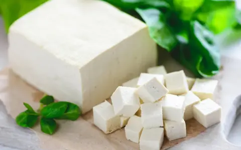 Kostka tofu, z czego jest zrobione, pokrojona w kostkę i ozdobiona listkami bazylii.