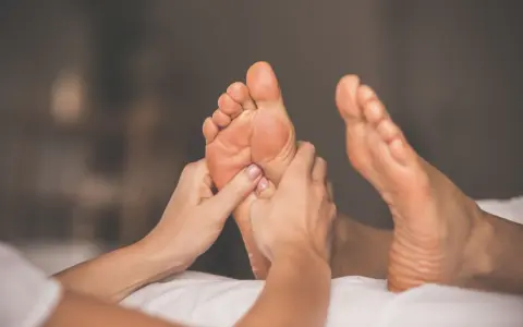 Hands giving a relaxing foot rub to a person lying on a white surface.
