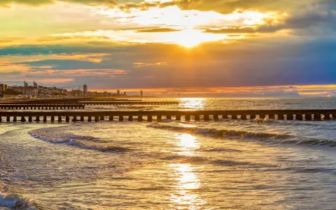 Tramonto dorato sul mare veneto, con moli che si estendono nell'acqua e una città all'orizzonte.