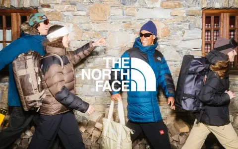 Cztery osoby w kurtkach The North Face, z plecakami i torbami, na tle kamiennej ściany. Jak rozpoznać podróbkę? Sprawdź detale!