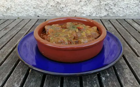 Goulash de ternera humeante en cazuela de barro, servido sobre plato azul. Un plato reconfortante listo para disfrutar.