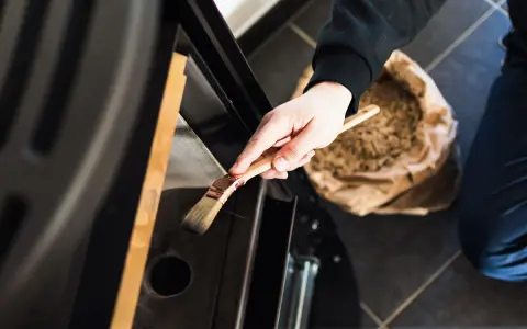 Mano che pulisce la stufa a pellet con un pennello. La manutenzione stufa a pellet ogni quanto è fondamentale per l'efficienza.
