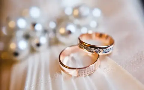 Dwa złote pierścionki z diamentami, symbolizujące 14 rocznicę ślubu, leżą na jedwabiu.