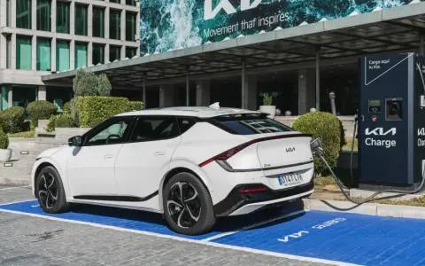 Un coche eléctrico blanco Kia EV6 cargando en un punto Kia Charge. Merece la pena un coche eléctrico por su tecnología y futuro.