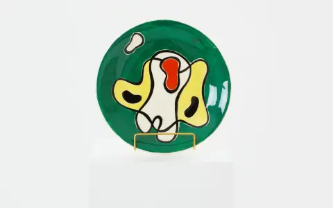 Assiette ronde verte ornée de formes abstraites noires, jaunes, rouges et blanches, dans le style de Roland Brice.