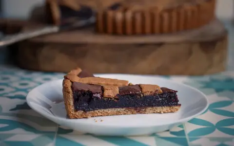 Una fetta di crostata al cioccolato, con la sua base dorata e il ripieno scuro e invitante, pronta per essere gustata.