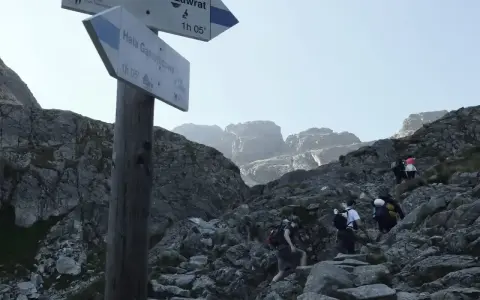 Grupa turystów wspina się po kamienistym szlaku w Tatrach. Tabliczka wskazuje kierunek na Zawrat.