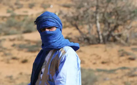 Ein Mann in traditioneller blauer Kleidung und Turban blickt aus der Wüste. Sind Marokkaner Araber? Ja, viele Marokkaner sind Araber.