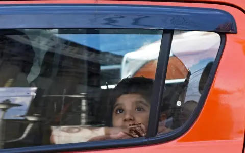 Niño mira por la ventana del coche, apoyado en el cristal, sin silla en el coche. Reflejos en el vidrio.