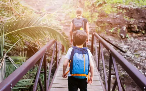 Bambini con zaini attraversano un ponte di legno in un sentiero lussureggiante, un'avventura perfetta per il tuo viaggio a Tenerife con bambini.