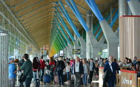 Ludzie z bagażami w nowoczesnym terminalu, jednym z wielu lotnisk w Europie, podziwiają architekturę z kolorowymi podporami.