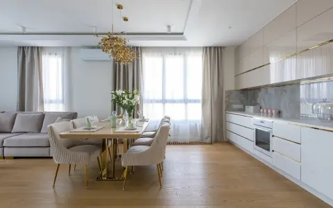 Elegancka kuchnia w stylu modern classic z jadalnią. Jasne meble, złote detale i wygodna sofa tworzą przytulną atmosferę.