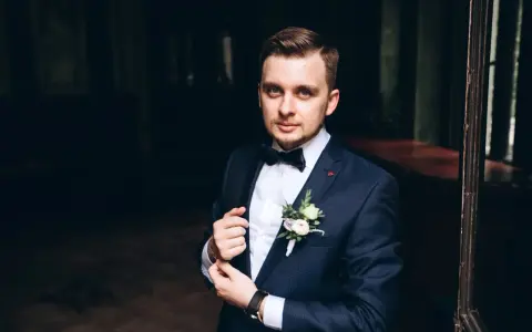 Elegancki mężczyzna w granatowym garniturze i muszce, z butonierką. Wygląda jakby przygotowywał się do ważnego wydarzenia, a nie do palenia.