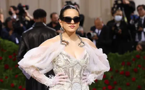 Rosalía deslumbrante en la Met Gala, con un vestido blanco adornado y gafas de sol vanguardistas.