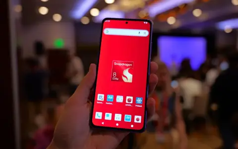 Dłoń trzyma smartfon z czerwonym tłem i ikoną Snapdragon 8 Elite. Widoczne ikony benchmarków, sugerujące testowanie wydajności procesora.