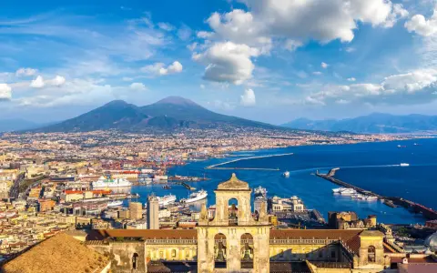 Vista di Napoli con il Vesuvio sullo sfondo, un porto vivace e un campanile antico. Un gioiello tra i siti UNESCO Campania.