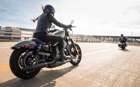 Kobieta w skórzanej kurtce i kasku jedzie na stylowym motocyklu dla kobiety. Wiatr rozwiewa jej włosy, a słońce odbija się od chromowanych elementów.