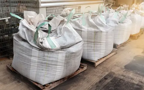 Rząd dużych worków big bag, każdy o pojemności ok. 1 m3, ustawionych na paletach.