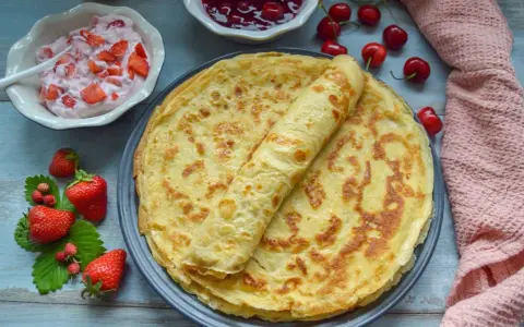Omas Pfannkuchen-Rezept: goldbraune Pfannkuchen auf einem Teller, dazu Erdbeerquark, Kirschmarmelade und frische Erdbeeren.