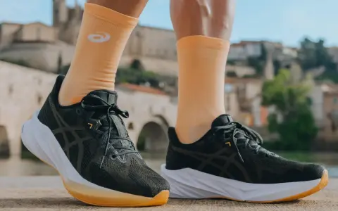 Biegacz w pomarańczowych skarpetkach z logo Asics i ciemnych butach tej firmy, gotowy do podboju miasta.