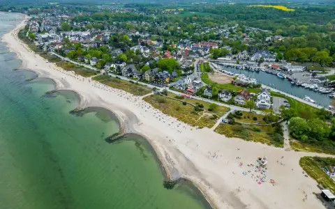 Luftaufnahme eines Strandes mit grüner Ostsee, Häusern und einem Yachthafen. Ein idyllischer Ort für ruhige Orte an der Ostsee.