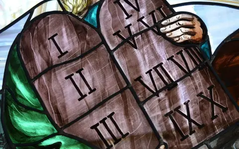 Witraż przedstawia kamienne tablice z wyrytymi cyframi rzymskimi, symbolizujące dekalog przykazania. Widoczne są cyfry I, II, III, IV, V, VI, VII, VIII, IX, X.