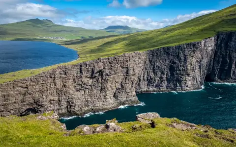 Scogliere imponenti e un lago blu intenso nelle Isole Faroe, dove gli abitanti vivono in armonia con la natura selvaggia.