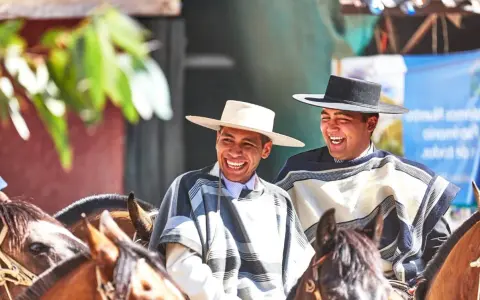 Deux huasos rient joyeusement à cheval, vêtus de ponchos traditionnels et de chapeaux.