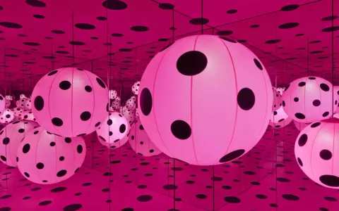 Salle infinie de Yayoi Kusama, remplie de sphères roses lumineuses à pois noirs, reflétées à l'infini par des miroirs.