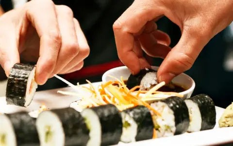 Ręce zanurzają sushi w sosie sojowym. Czy sushi można jeść na drugi dzień? To zależy od świeżości składników i sposobu przechowywania.