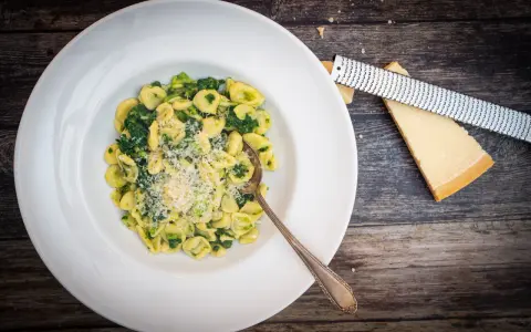 Orecchiette mit Cime di Rapa, frisch geriebenem Parmesan und einem Löffel auf einem Holztisch.