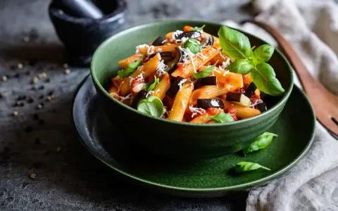 Un plato de pasta alla norma, con penne, berenjena, salsa de tomate y albahaca fresca, espolvoreado con queso rallado.