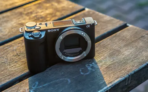 Czarny aparat Sony Alpha ZV-E10 bez obiektywu leży na drewnianym stole, oświetlony ciepłym światłem zachodzącego słońca.