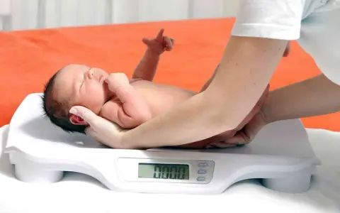 Neonato su bilancia, monitoraggio del calo fisiologico. Le mani sorreggono il piccolo durante la pesata.
